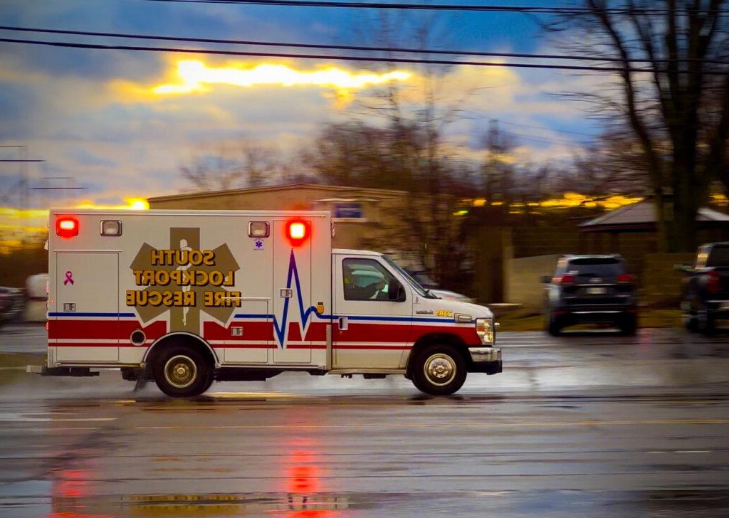 Ambulance in action, lights flashing, wet road
